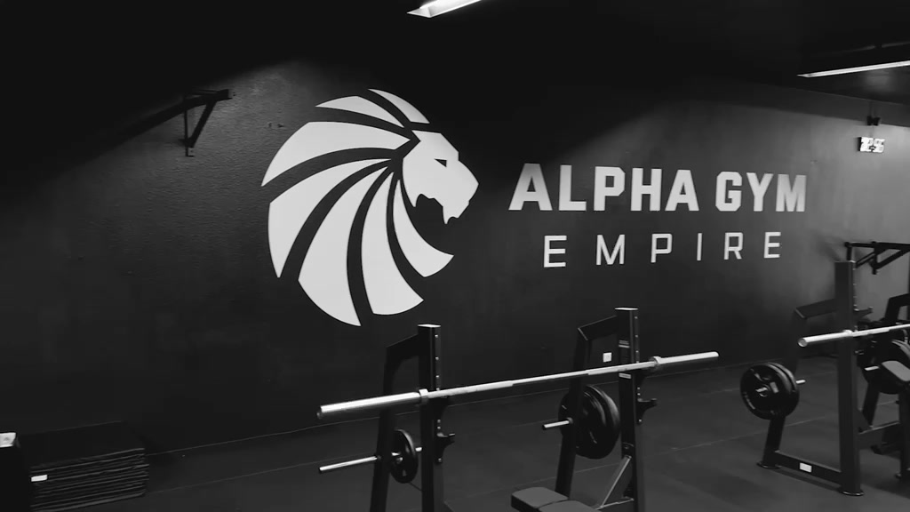 Alpha Gym Empire Logo an der Studiowand mit Langhantel